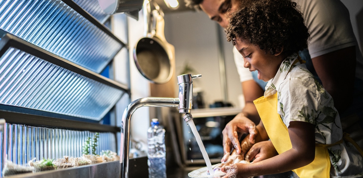 A child and an adult washing dishes together at a kitchen sink.
